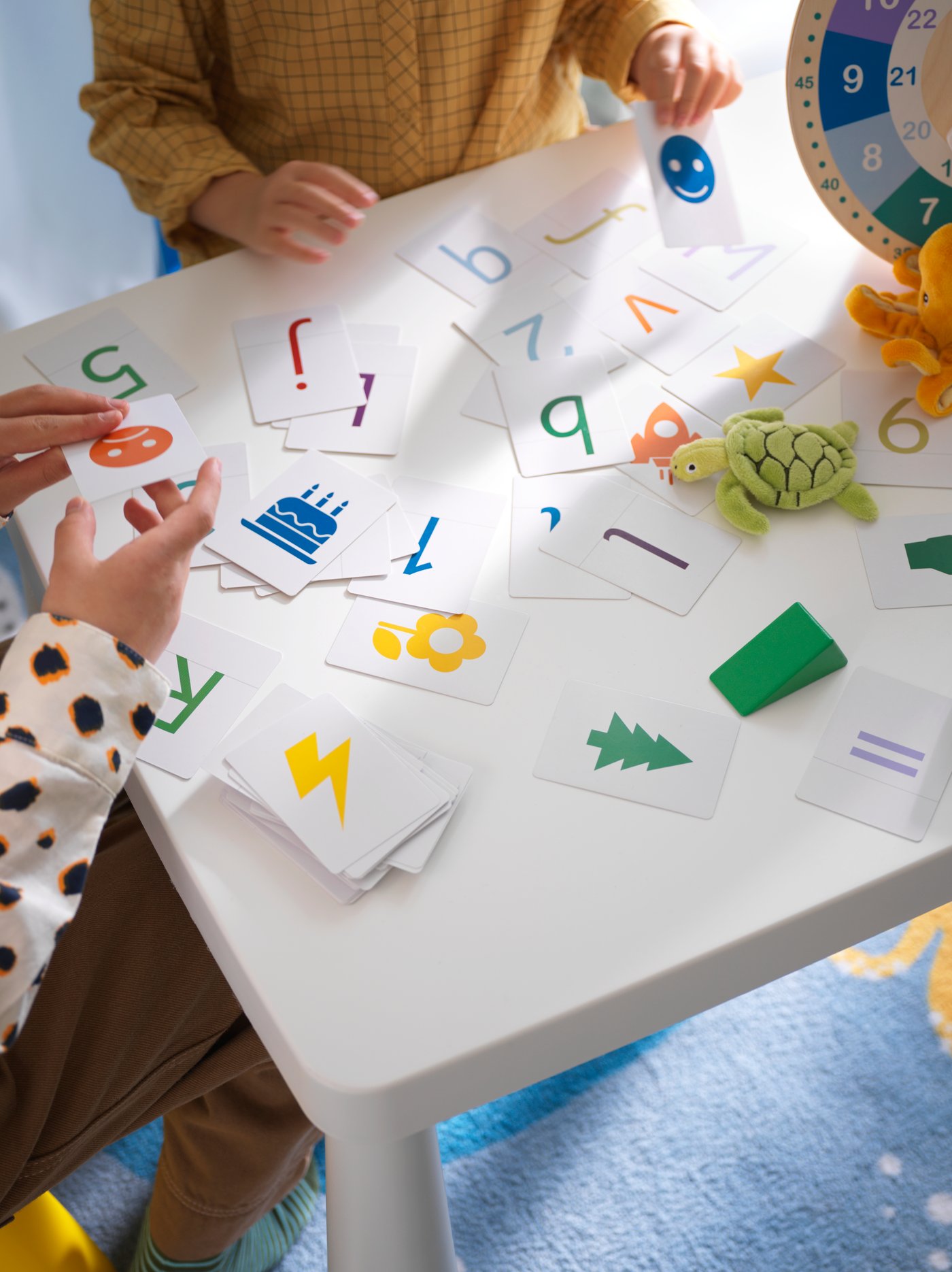 Close up shot from above of table where two children are playing with UNDERHÅLLA cards on white table.