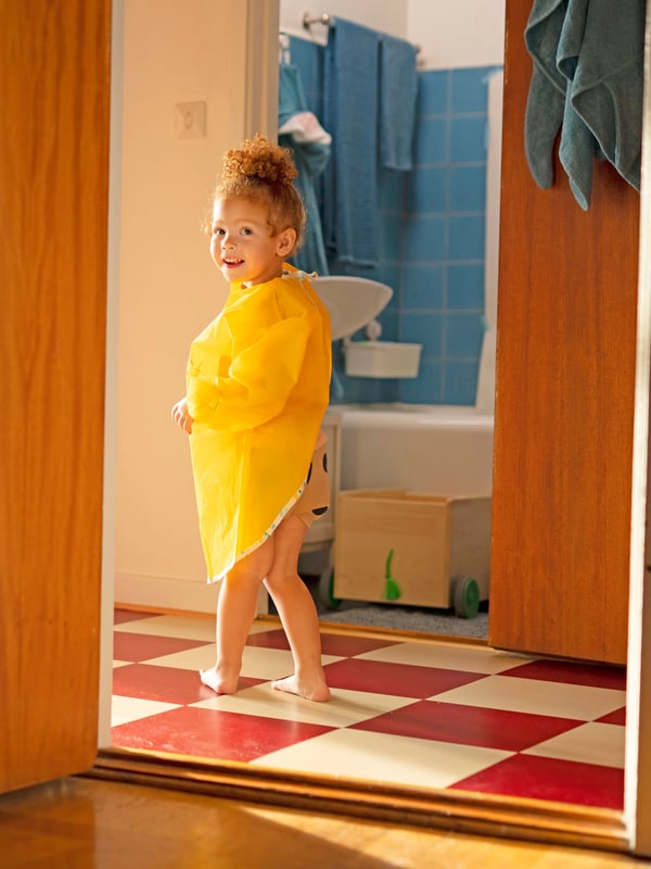 Un bambino con un grembiule giallo di MÅLA in piedi davanti al bagno.