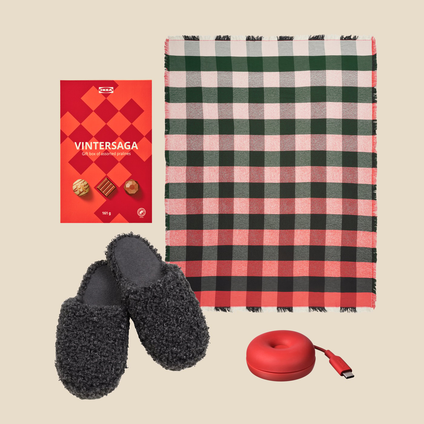 A box of VINTERSAGA chocolate pralines next to VINTERFINT slippers, a VINTERFINT throw and a red wireless charger.