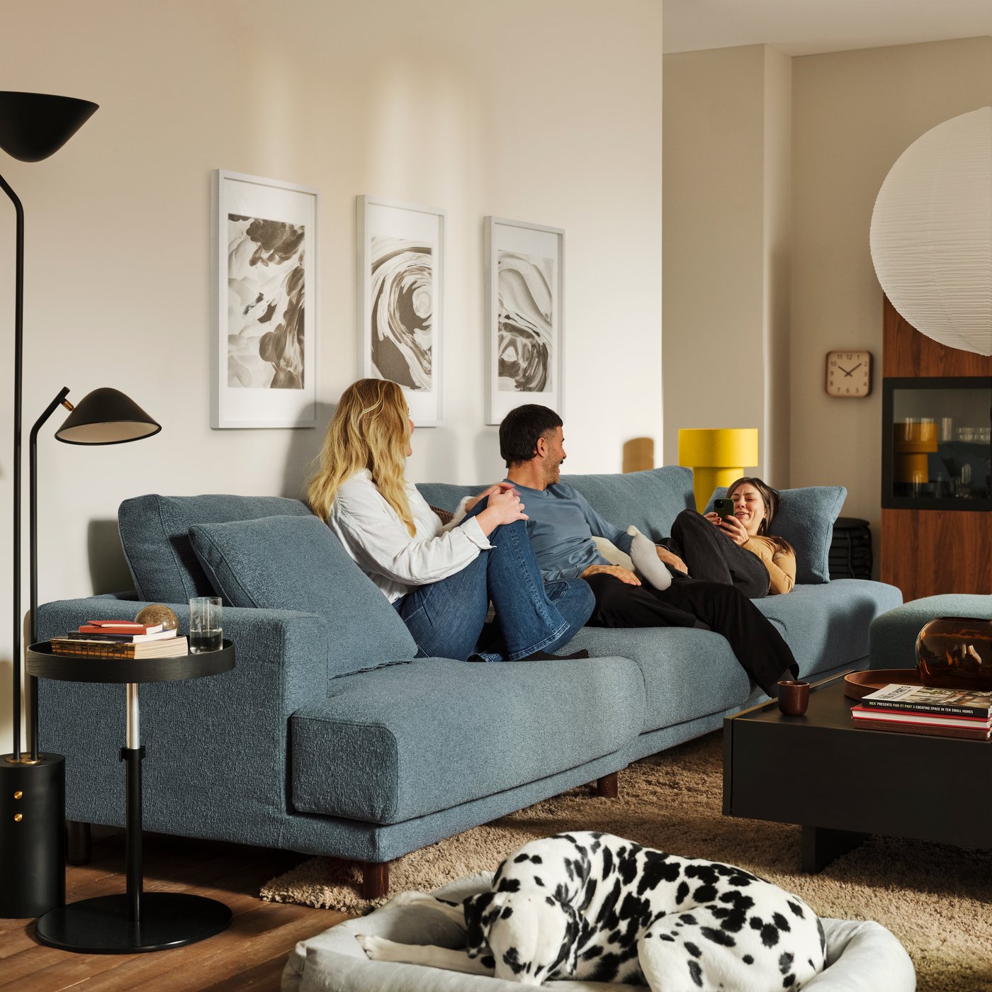 Three people lounge on a dark grey-blue UPPÅKRA 4.5-seat modular sofa near a TRANERED coffee table and a TRANERED side table.