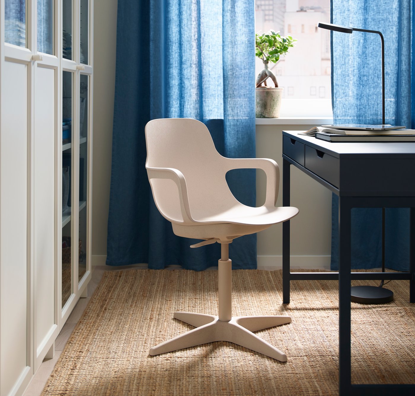A beige ODGER swivel chair in the home office with blue curtains hanging for the window.
