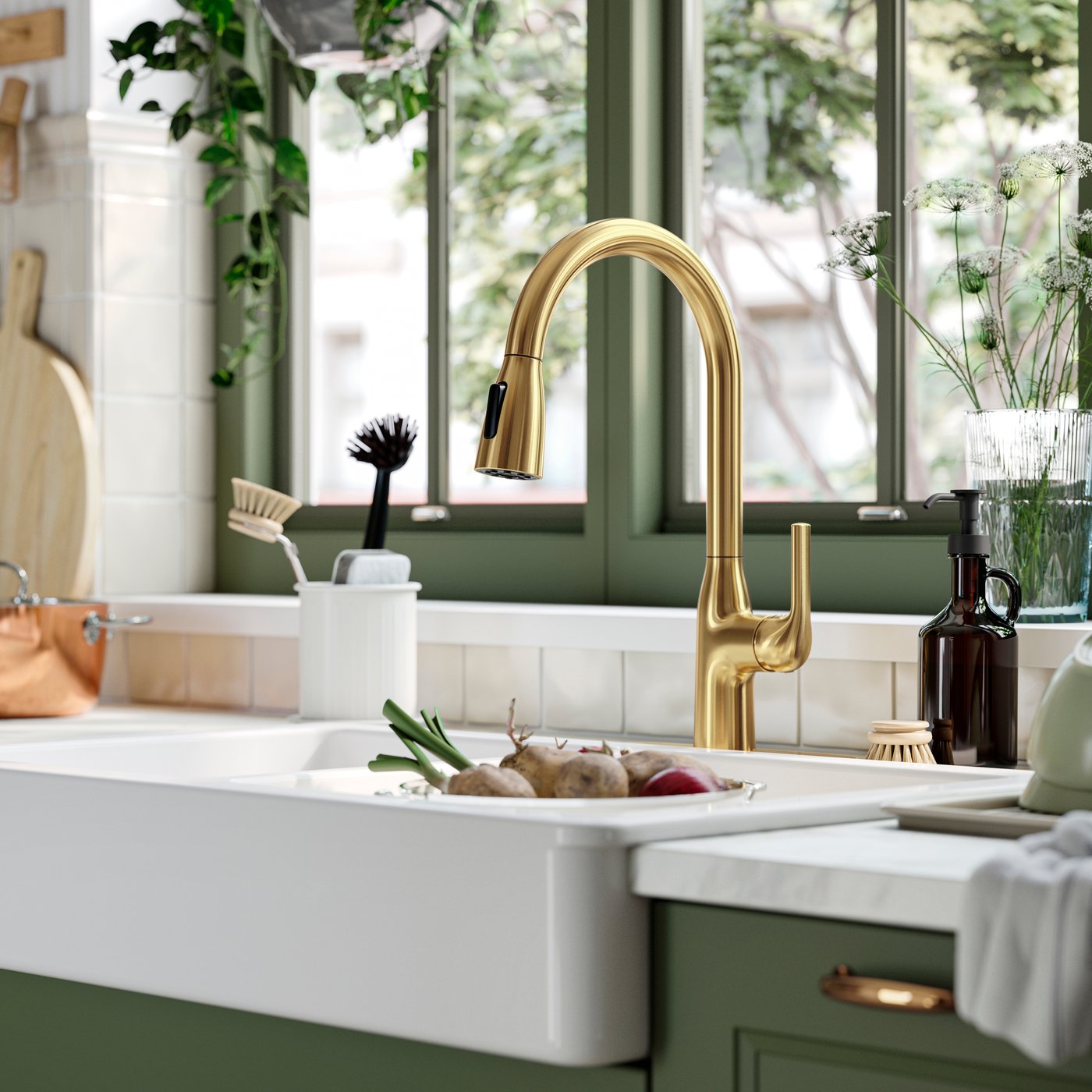 A MACKSJÖN kitchen mixer tap with a pull down-spray function in brass above a white wash basin in a green kitchen.