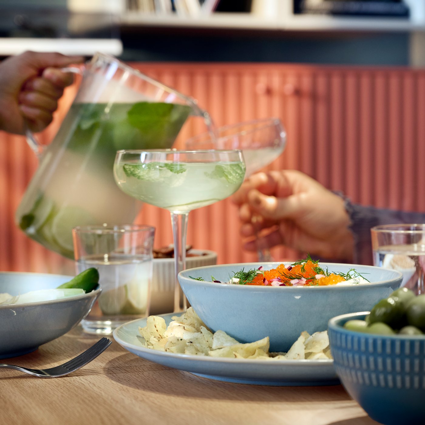 Iemand schenkt een feestelijk drankje in het glas van iemand anders en op tafel staat lichtblauw FÄRGKLAR-servies.