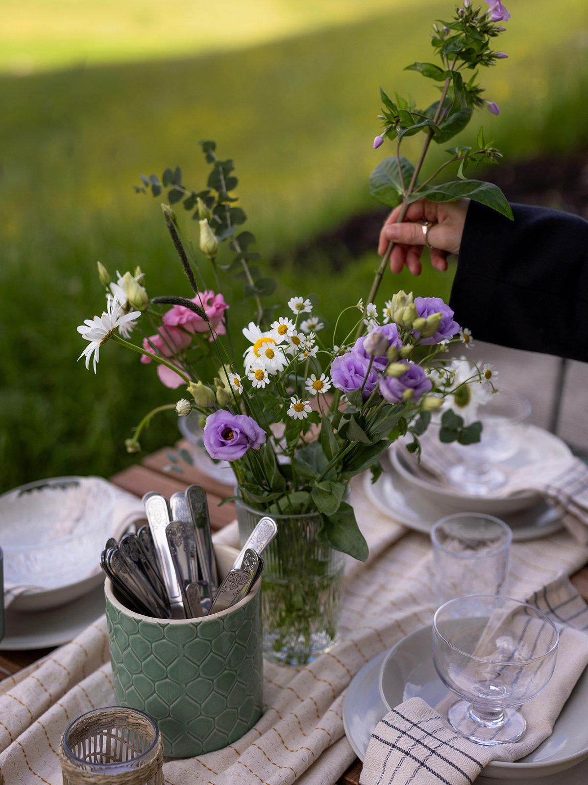 Ett utomhusdukat bord med blommor och vitt och beige porslin.