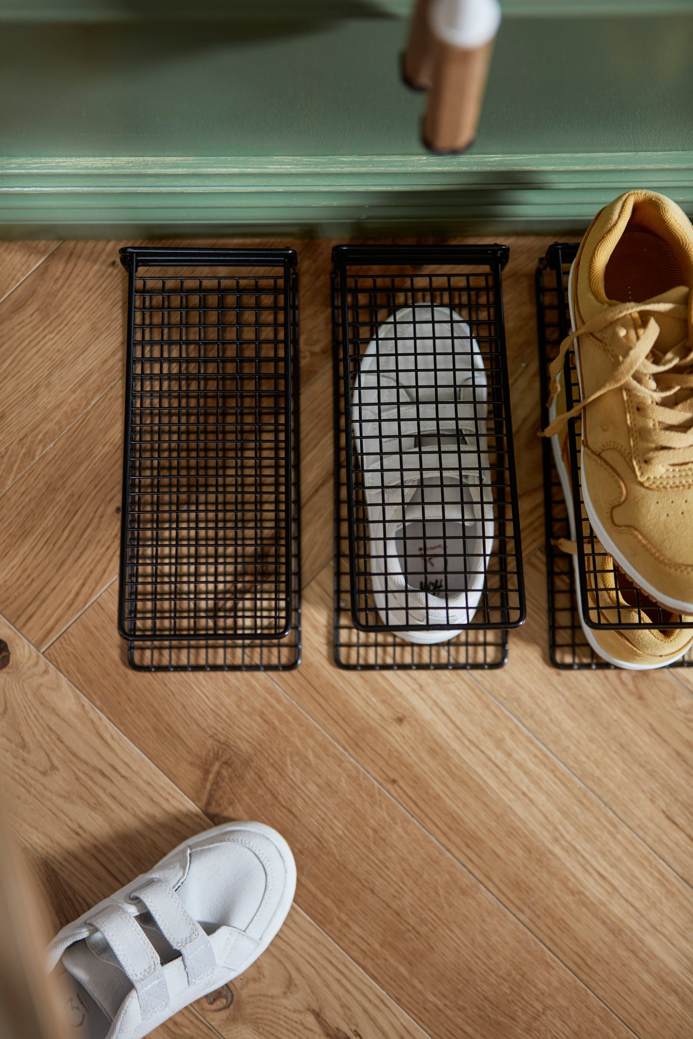 Trois range-chaussures SKOSTALL noirs sont posés sur le sol d’une entrée. Un organisateur contient une paire de chaussures de course.
