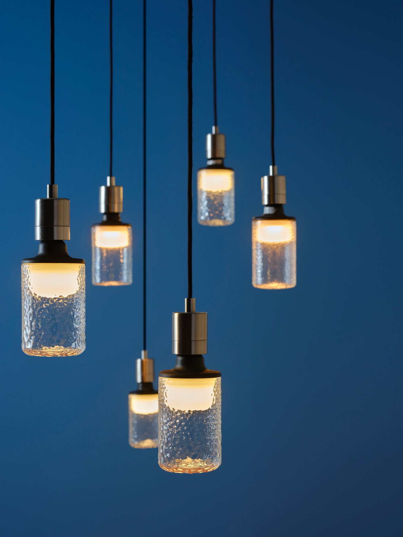 A grouped display of MOLNART tube-shaped, patterned-clear-glass LED bulbs, hanging in cords at different heights.
