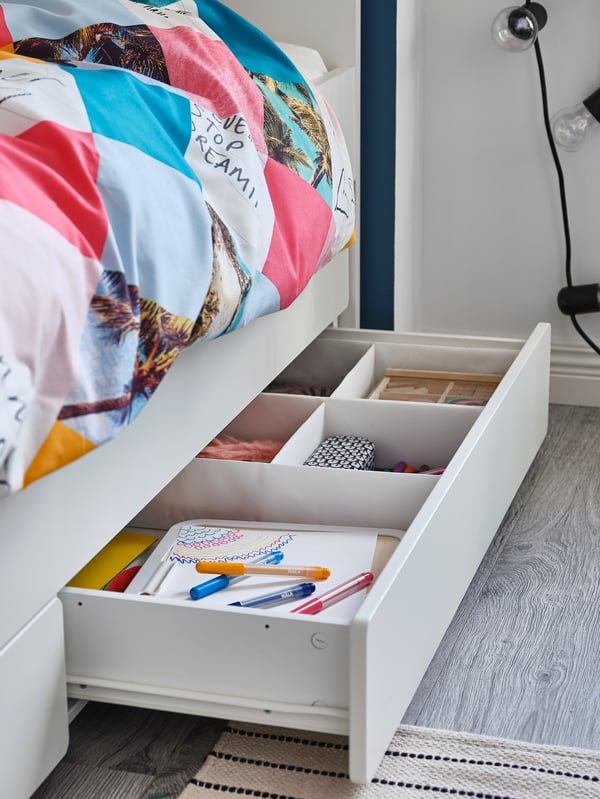 A SLÄKT bed with underbed and storage stands in a child’s bedroom. A drawer is pulled out from under the bed.