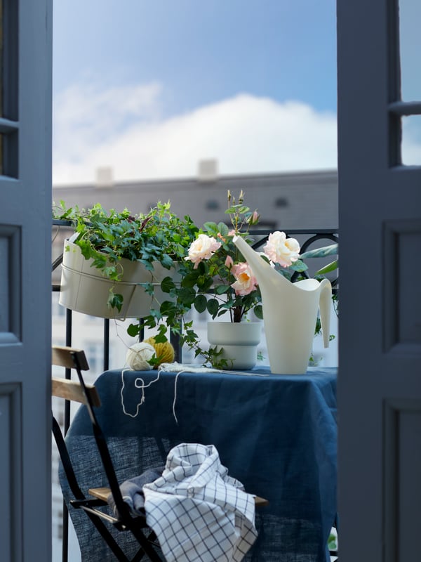 Small outdoor dining set with flow box hanging from railing, beige flower pot on table with white watering can beside
