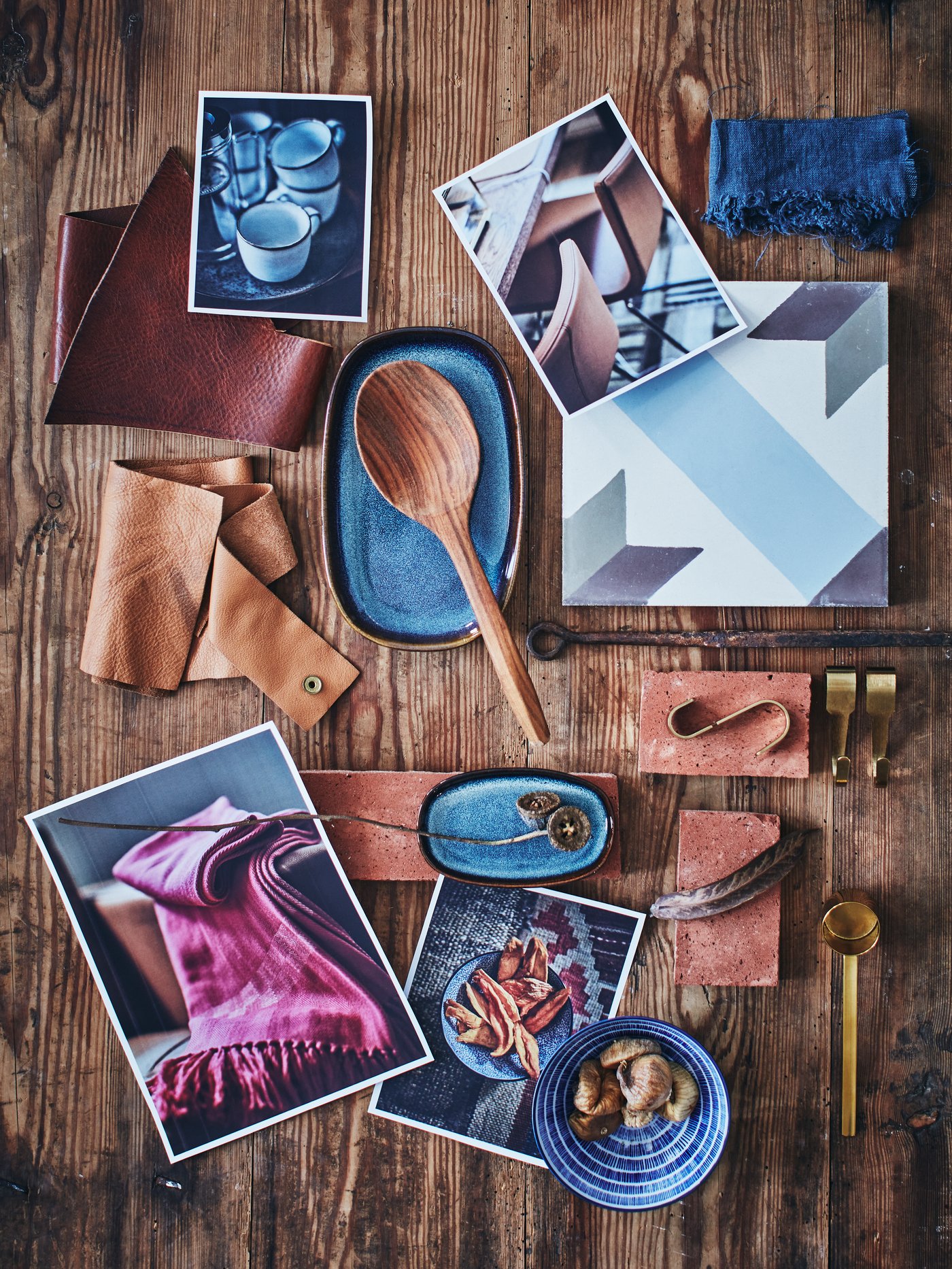 A moodboard of a wooden spoon, dark blue oval dish, some photographs, pieces of leather and fabric, hooks and a kitchen tile.