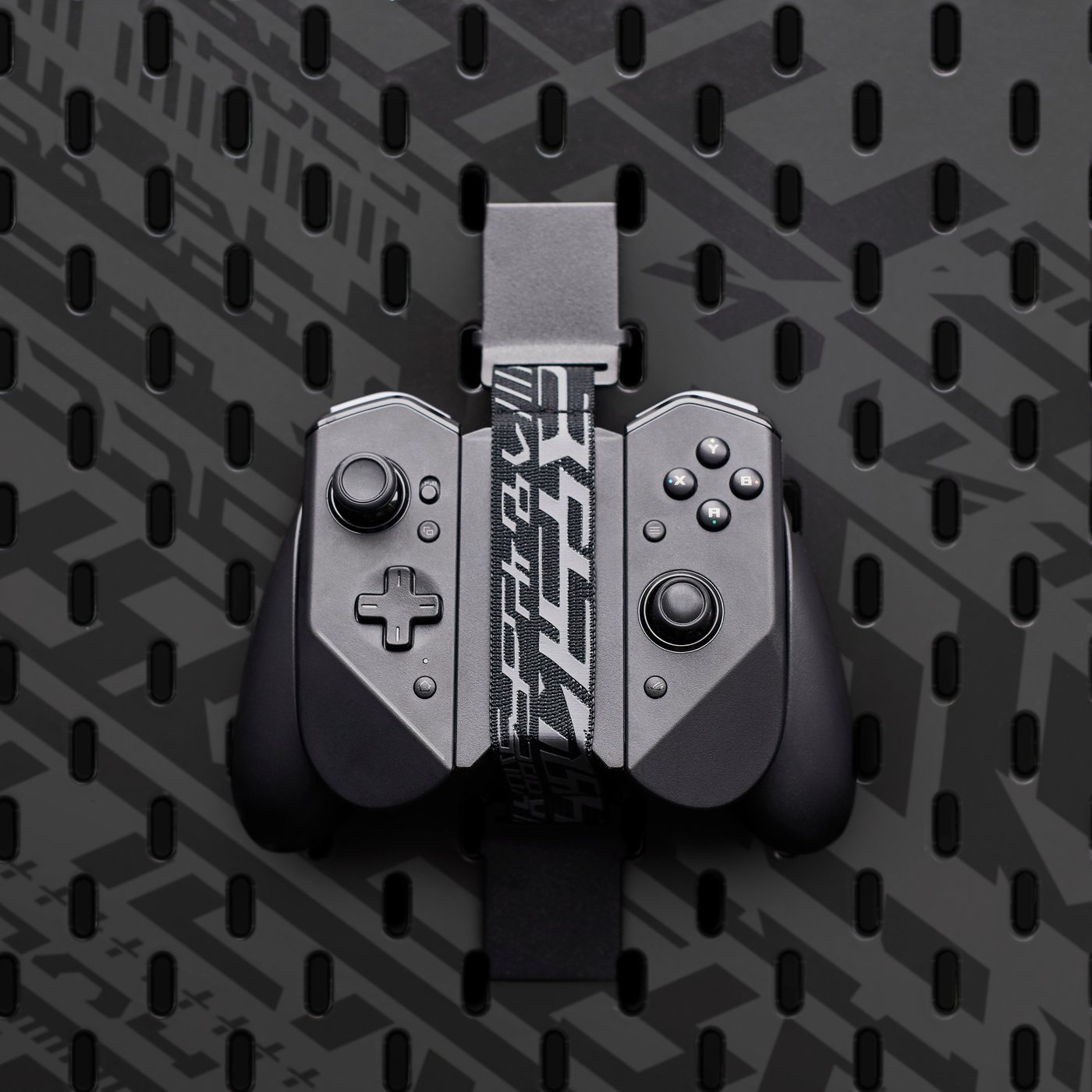 An IKEA UPPSPEL elastic strap holding a game controller on a black pegboard.