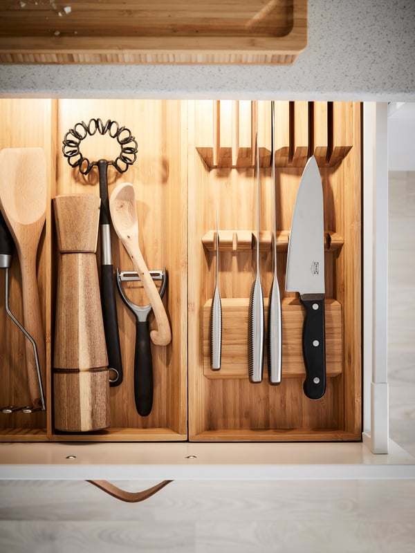 Knives and cooking utensils stored in wooden utensils trays inside a drawer.