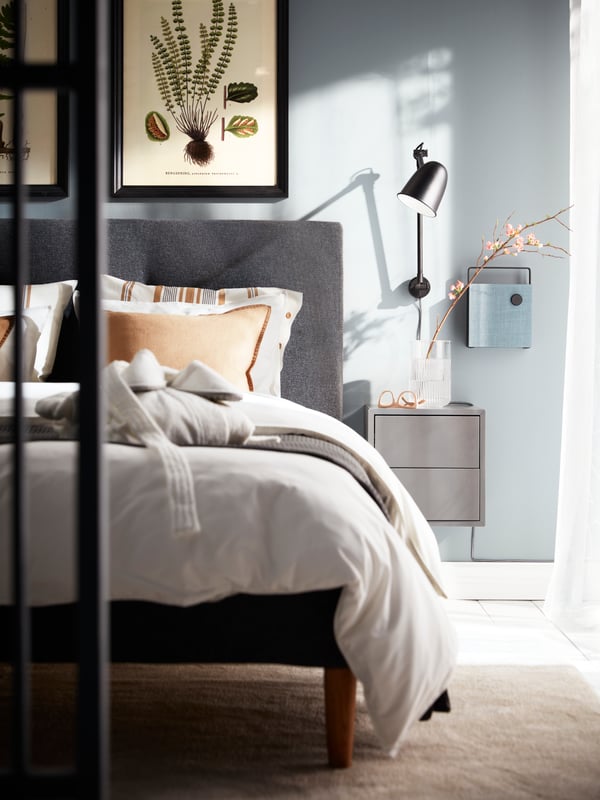 A black SKURUP wall lamp, a dark grey EKET cabinet and a Bluetooth speaker mounted on a wall beside a dark grey IDANÄS bed.