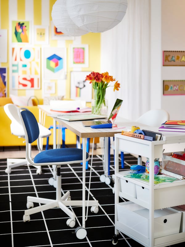 A colourful room with swivel chairs by side-by-side desks, all wheeled and all placed on a graphic-pattern SVALLERUP rug.