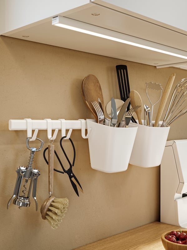 IKEA SUNNERSTA white rail with 4 hooks and 2 containers holding some cutlery and a silver-colour IDEALISK corkscrew in the kitchen.