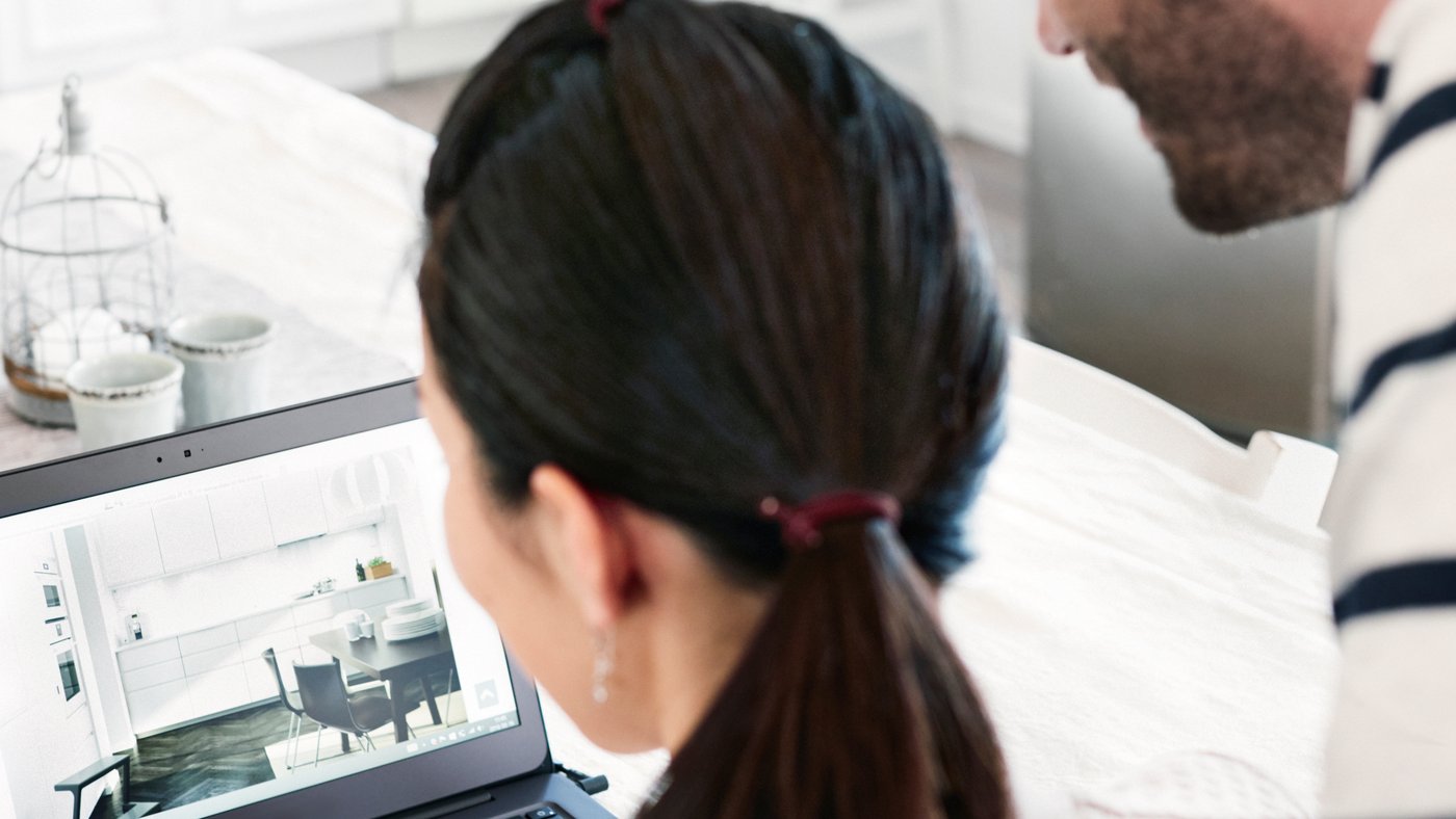 Two people are looking at a laptop in a kitchen.