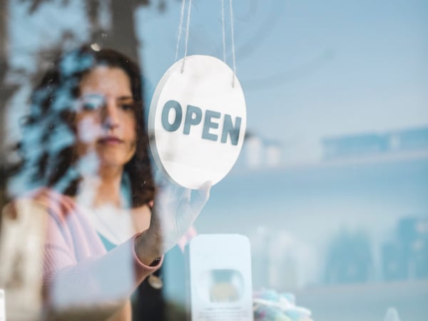 A woman in a room holding up an OPEN sign.
