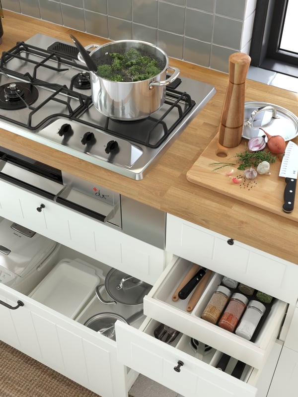 An IKEA 365+ pot with lid on a gas hob with fish grill, plus open kitchen drawers below with pots, oven dishes and spices.