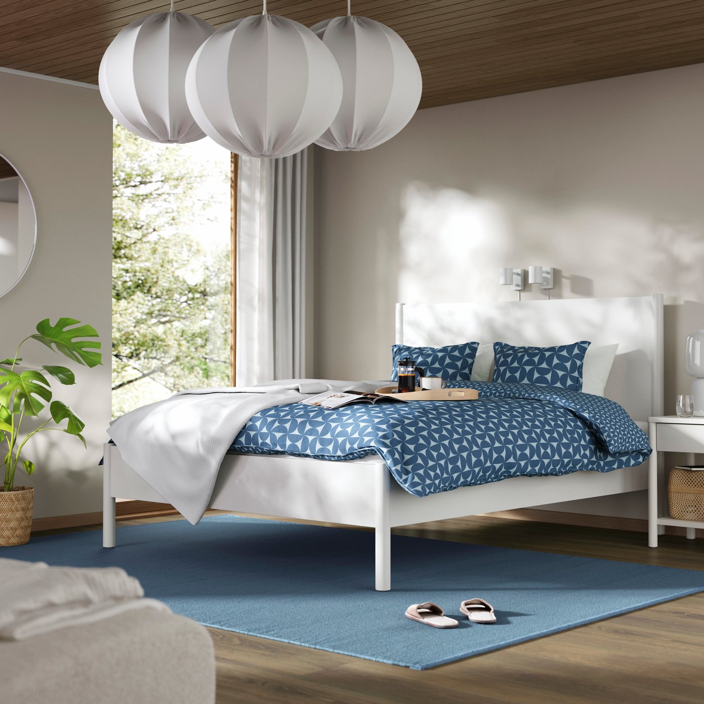 Bright bedroom with a white bed, blue patterned bedding and large round pendant lights.
