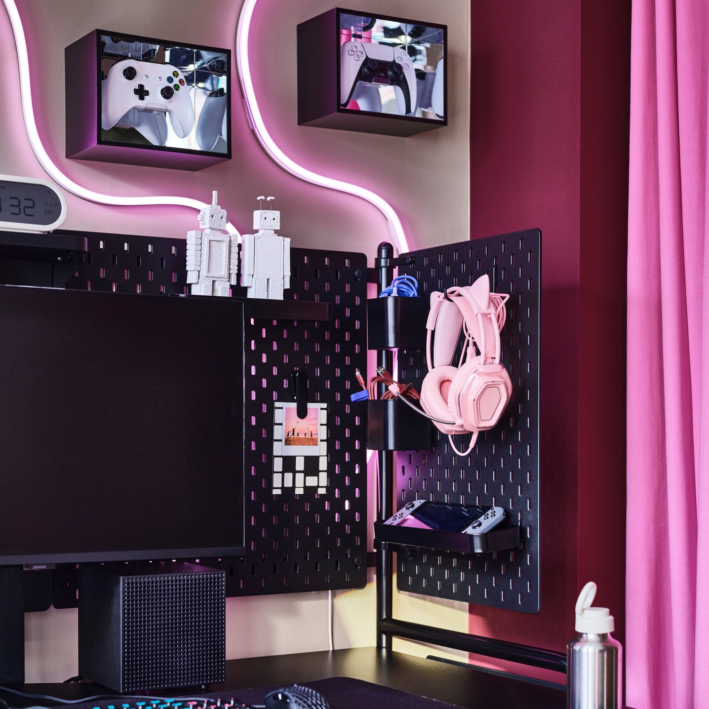 A corner with pink accents and YXSTABY display boxes framing a black FRÖSKELÅS gaming desk with neatly arranged accessories.