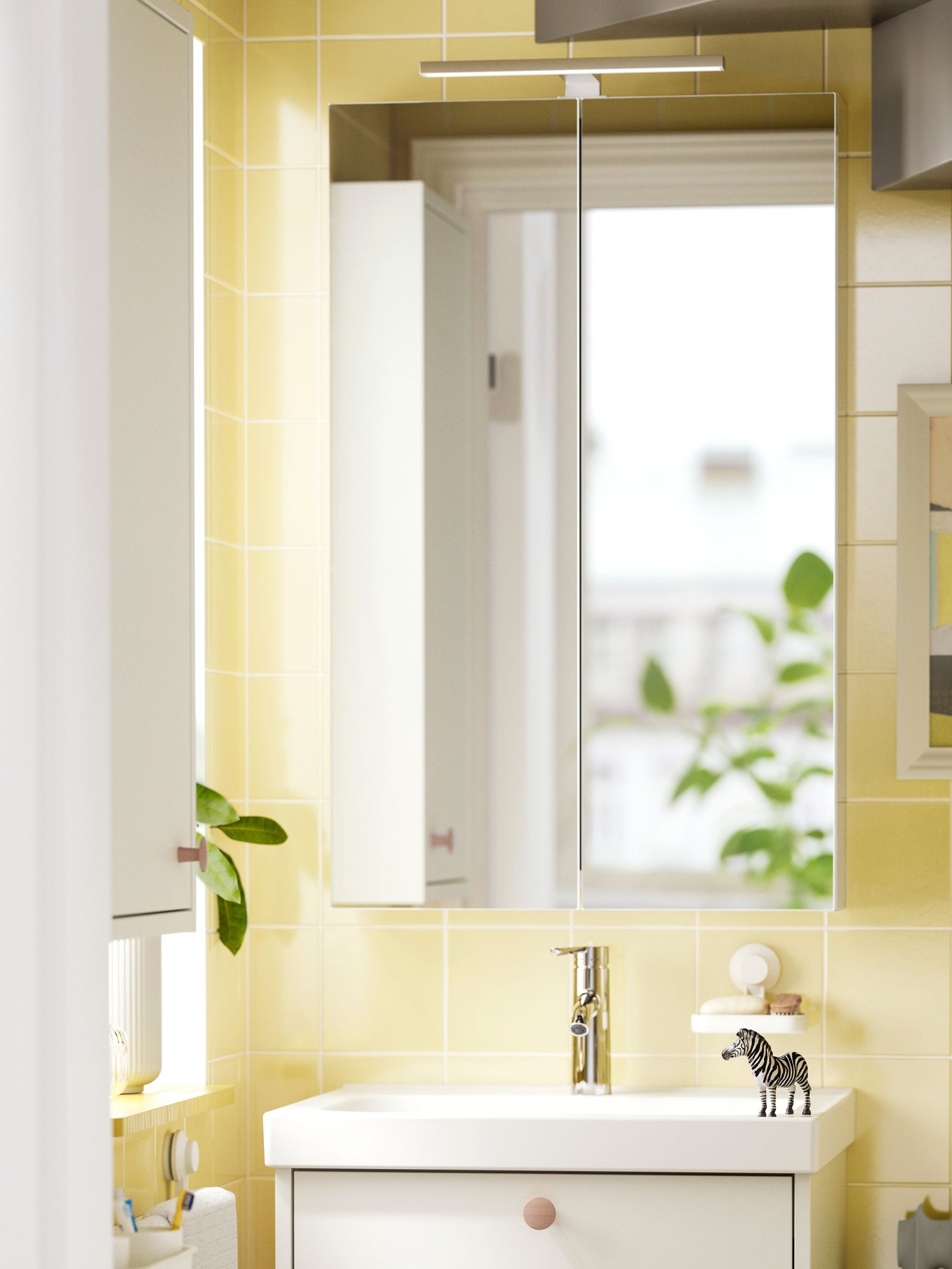 A bright and yellow tiles bathroom with LETTAN mirror cabinet, a white sink and vases with green branches and deco objects.