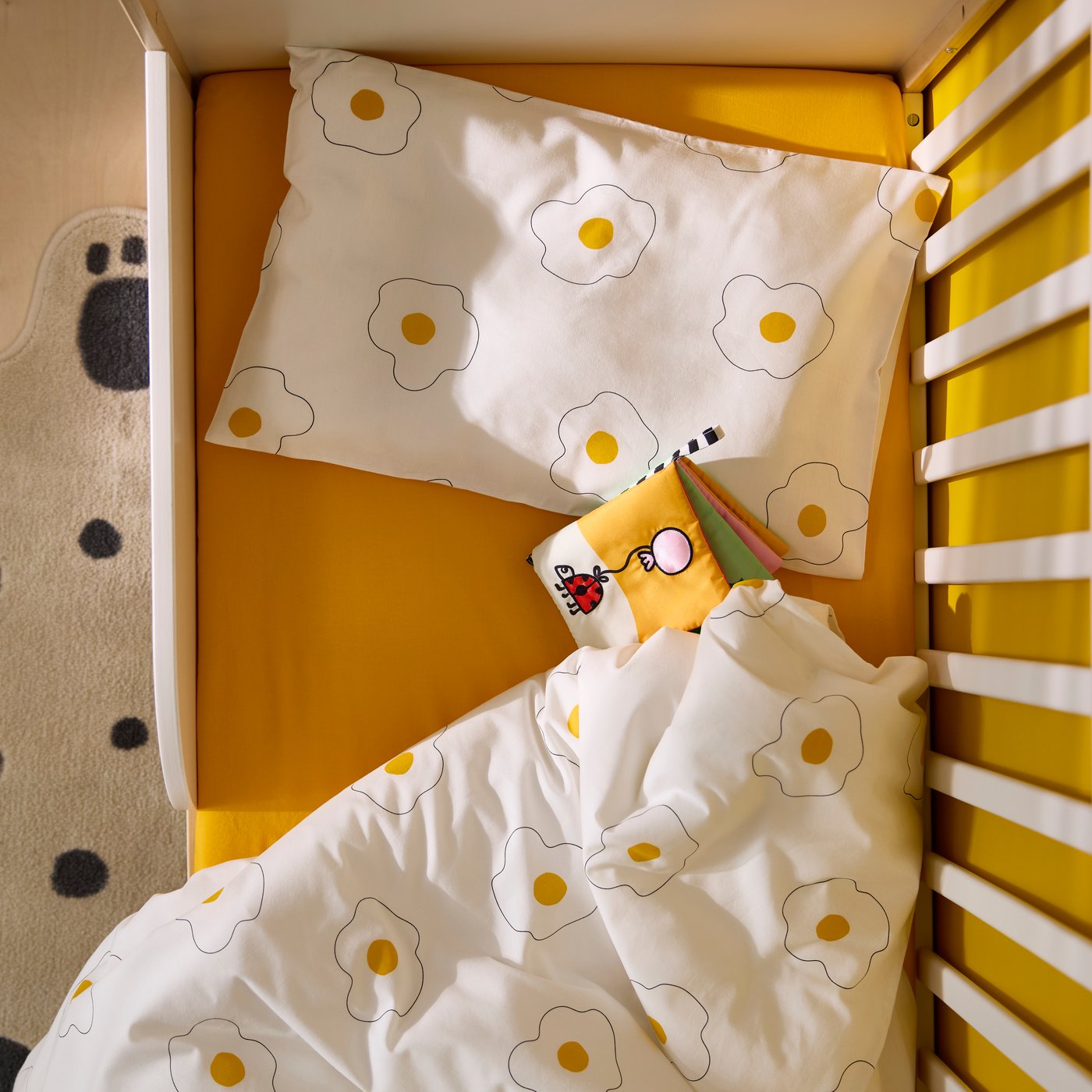 Bird’s-eye view of children’s bed with yellow sheet and white bed linen with fried-egg theme.
