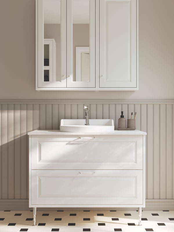 A bathroom has a white TÄNNFORSEN wash-stand with two drawers on metal legs, with a white countertop and a mirror cabinet.