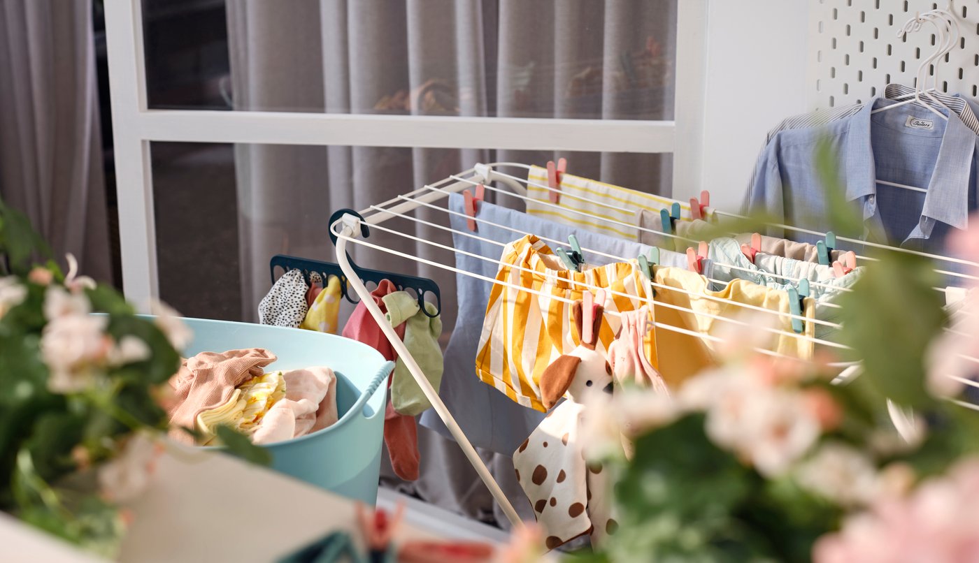 A white JÄLL drying rack with clothes held by clothes pegs and a hanger with 8 grip clips, plus a flexible laundry basket.