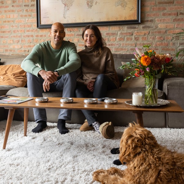 Couple smiling, sitting on their neat sofa, with their dog at their feet.
