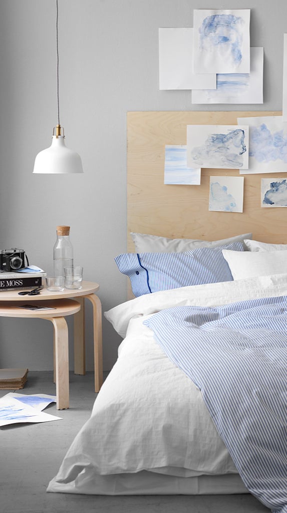 Dormitorio con ropa de cama blanca y azul y una lámpara colgante blanca.