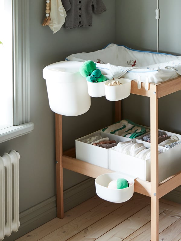 A SNIGLAR changing table with a changing mat and ÖNSKLIG storage baskets attached to the side holding baby care items.