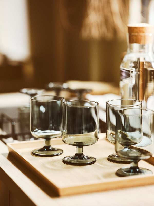 An IKEA 365+ carafe with stopper containing water behind four grey OMBONAD goblets placed on a bamboo OSTBIT tray.