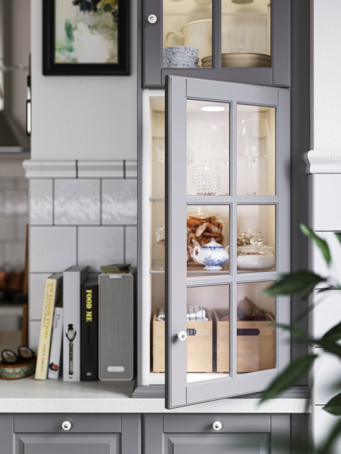 Base cabinets with grey BODBYN fronts, wall cabinets with glass doors and integrated lighting, plus cookbooks on a worktop.