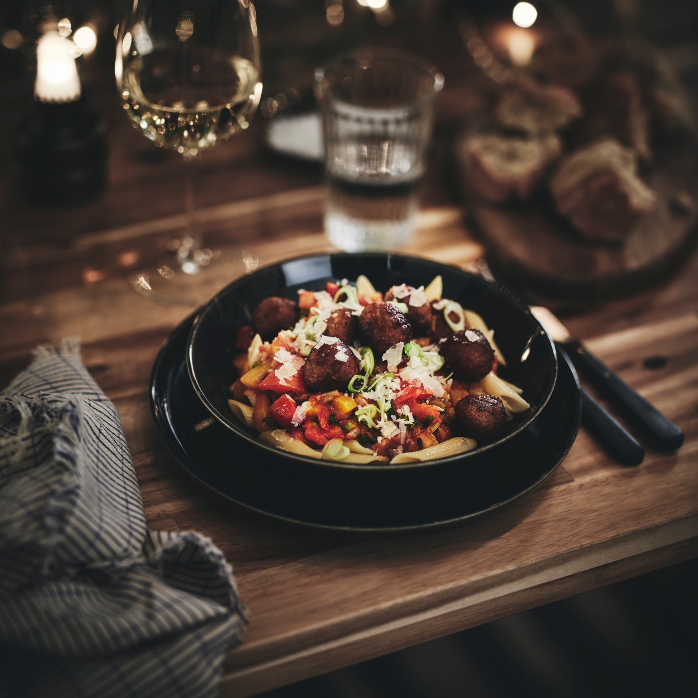 A pasta and meatballs dish in a GLADELIG bowl on a table surrounded by a napkin, water glass and a glass of sparkling drink.