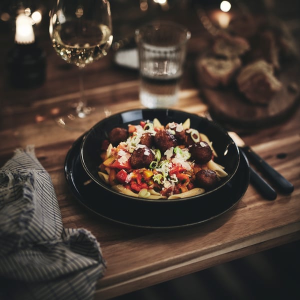A pasta and meatballs dish in a GLADELIG bowl on a table surrounded by a napkin, water glass and a glass of sparkling drink.