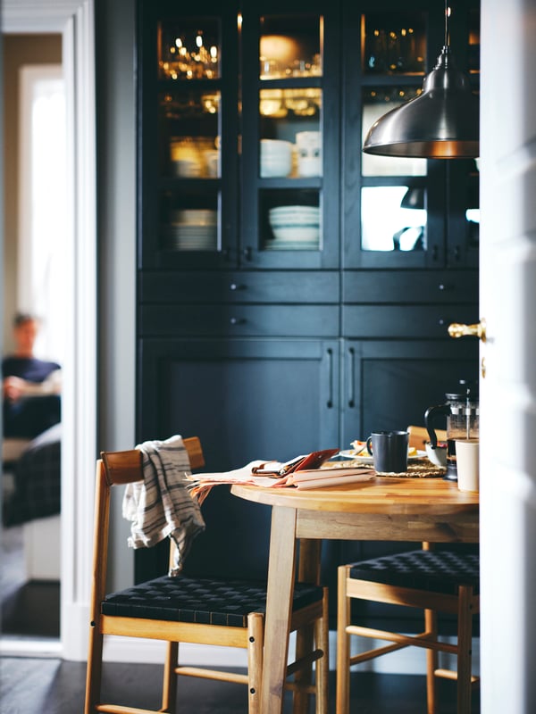 Kitchen cabinets with black stained LERHYTTAN doors behind an acacia NACKANÄS table and two NACKANÄS chairs.