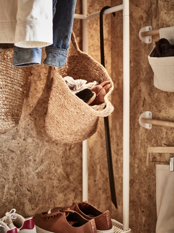 Two jute TOLKNING hanging baskets on a white coat rack with shoe storage, plus two birch wall rails with hanging storage.