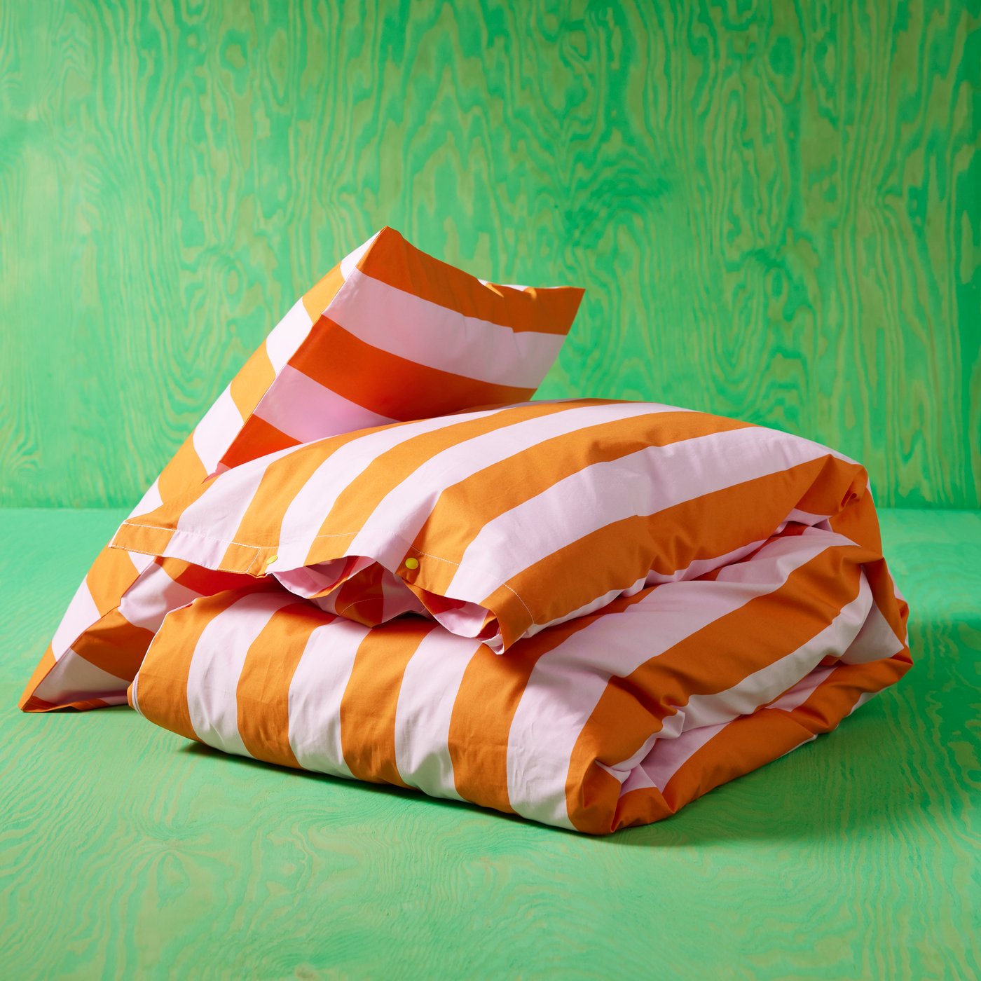 Eine orange-rosa gestreifte SLÅNHÖSTMAL Bettwäsche vor einem grünen Hintergrund