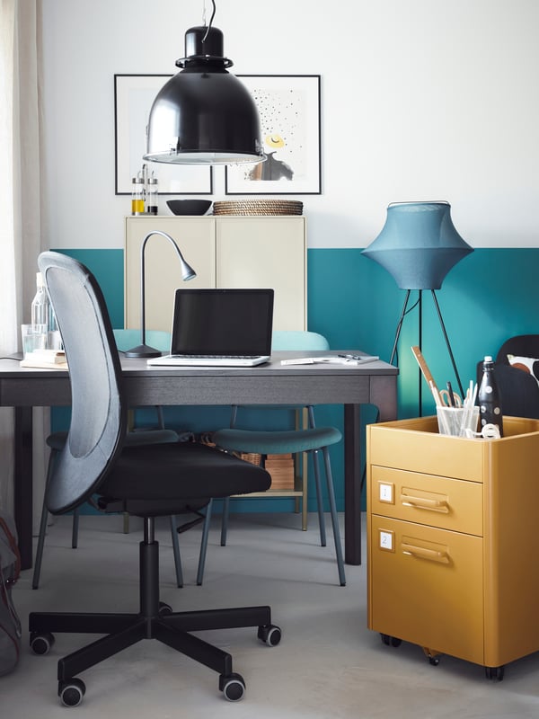 An EKEDALEN table set up for working, with a laptop on it, a yellow drawer unit beside it and a work chair in front.