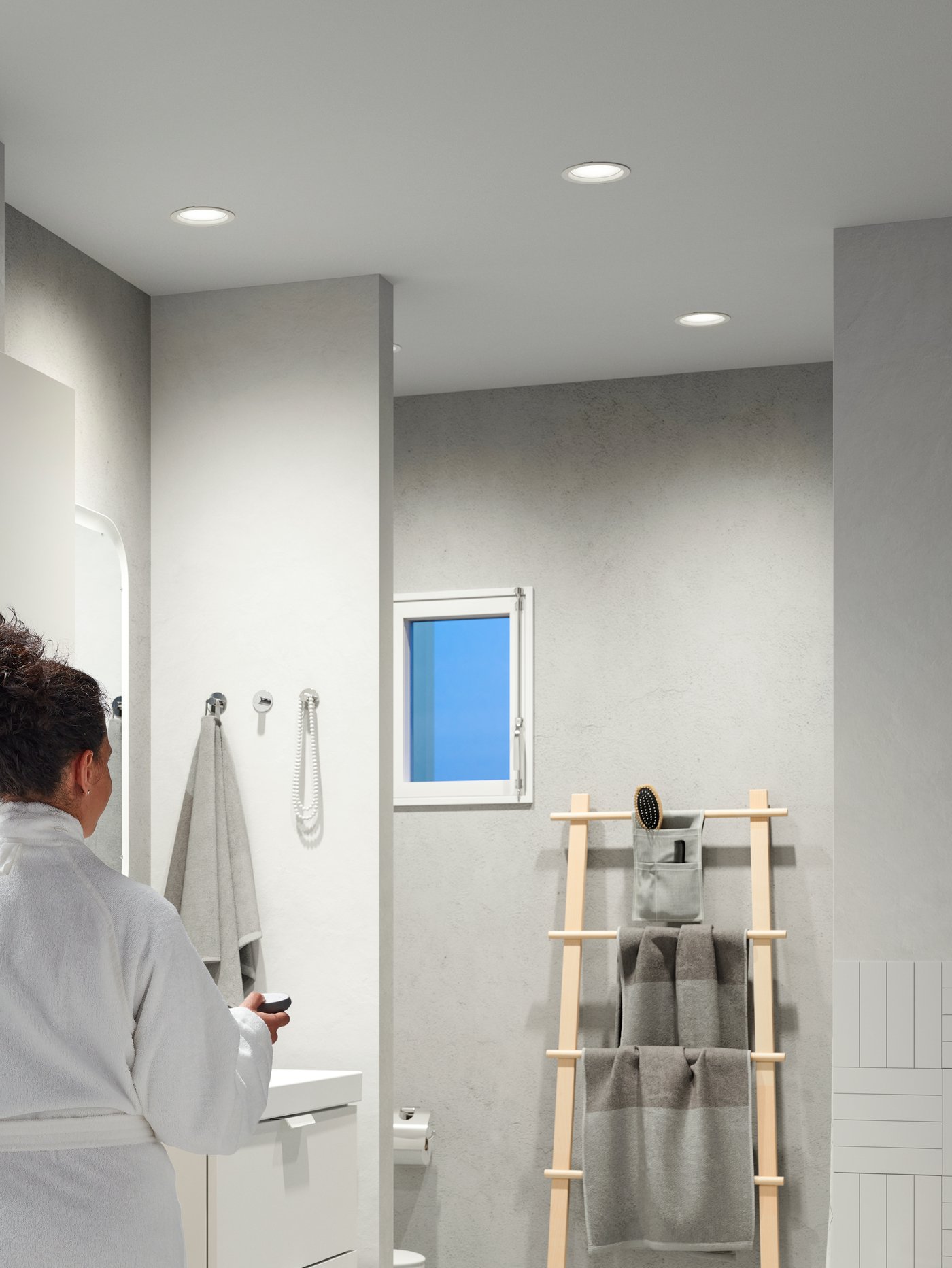 A girl holds a TRÅDFRI remote and controls ceiling spotlights with TRÅDFRI LED bulbs that give a slightly dimmed light.