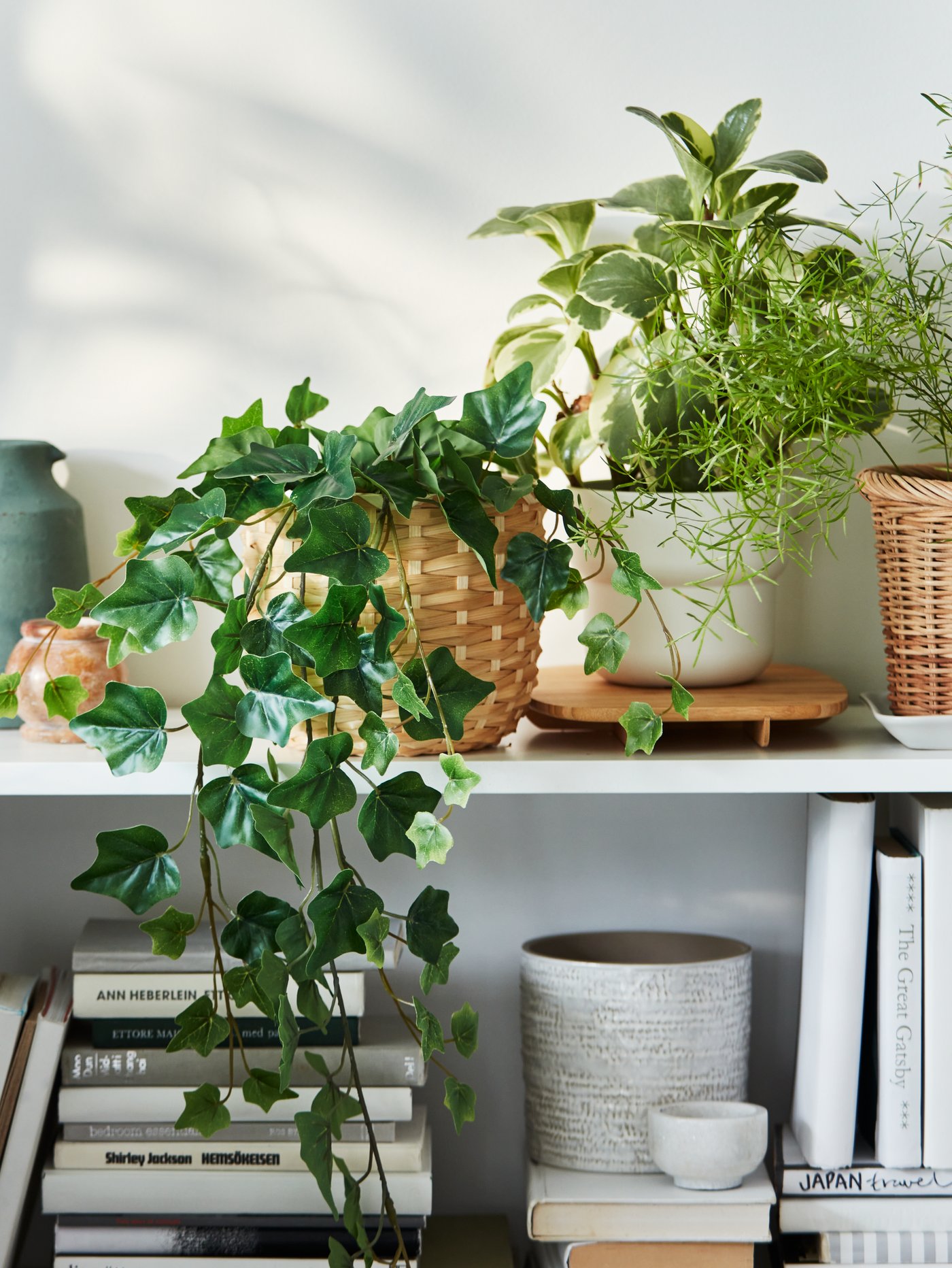 A section of a white BILLY bookcase filled with a mix of books and FEJKA artificial plants in various plant pots.