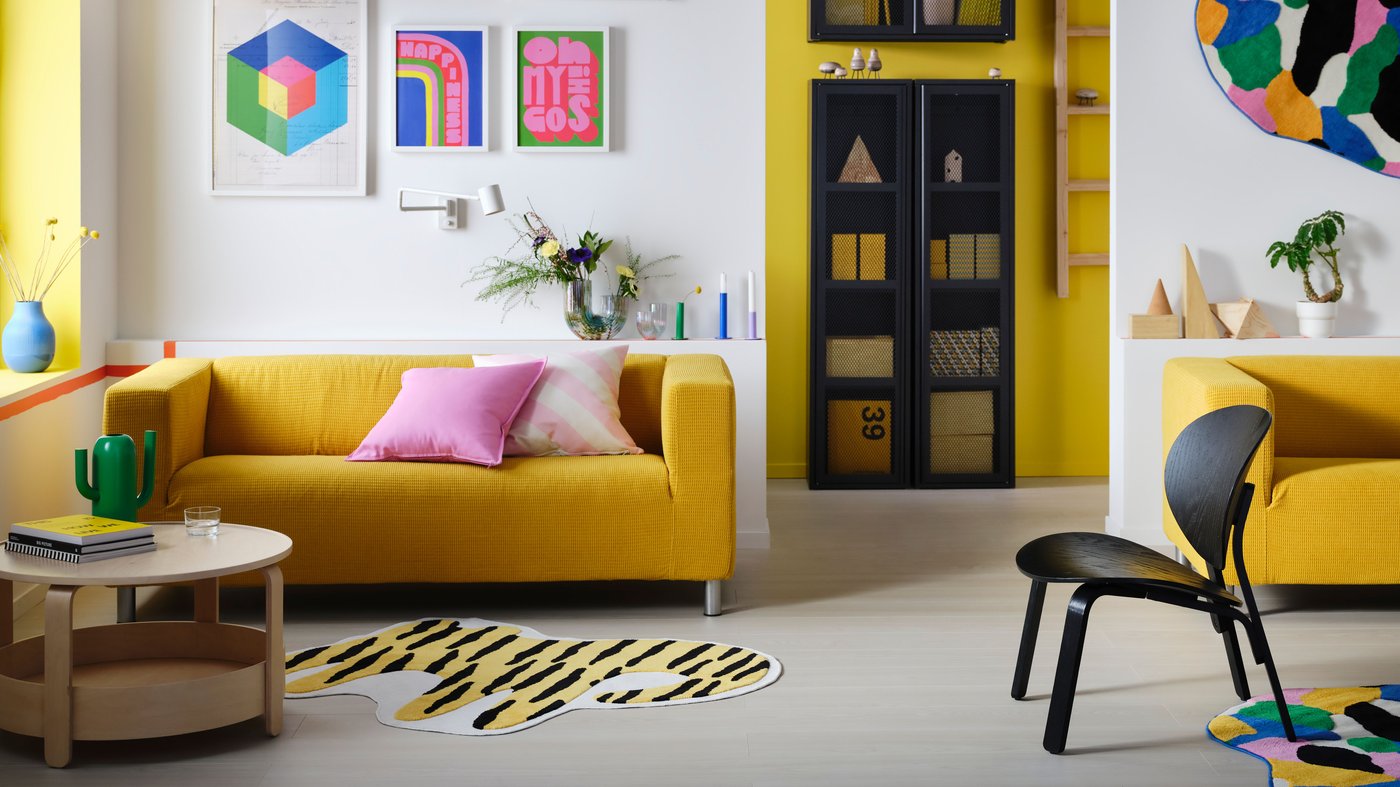 A yellow KLIPPAN sofa with two cushions on top in a colorful living room.