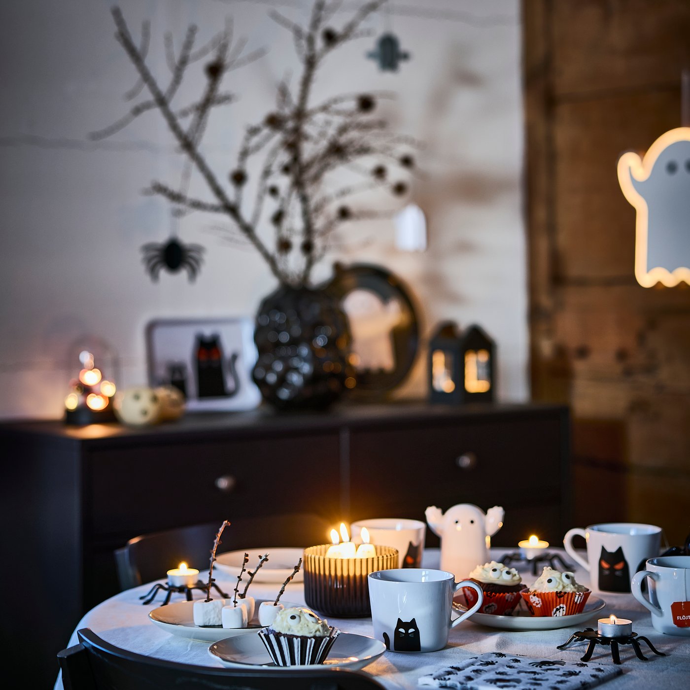 A dining table set for a Halloween gathering using four KUSTFYR mugs, side plates, baking cups and lit scented candles.