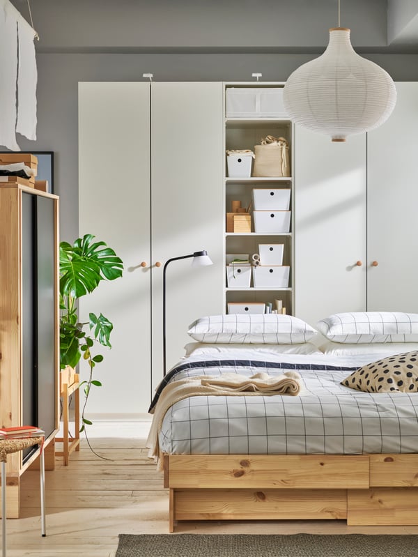 Schlafzimmer in Beige und Weiß mit Bett aus Naturholz und beigem Bettzeug. Kombination von weißen PLATSA Schränken im Hintergrund.