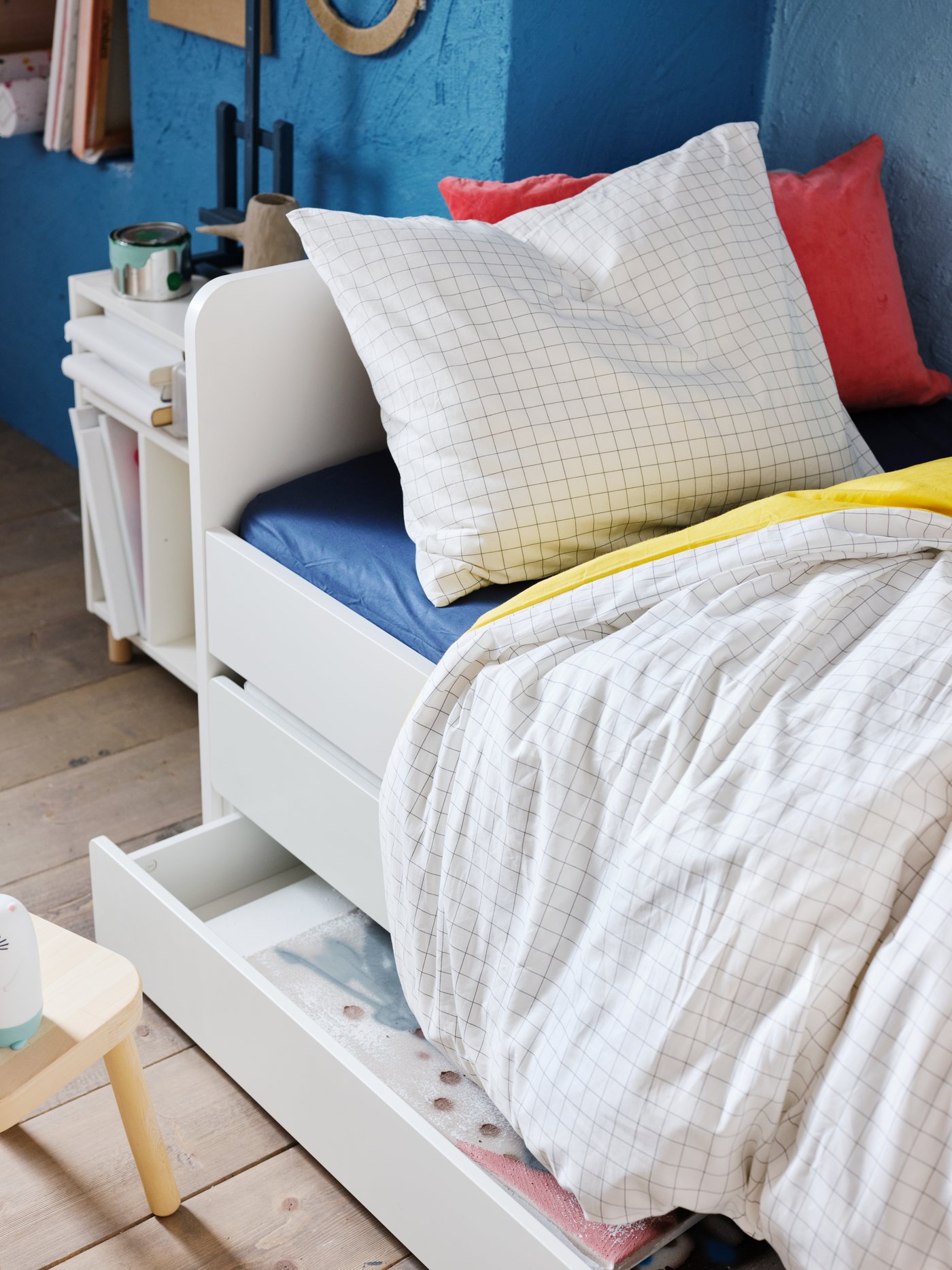 A white chidren's bed in a blue room with wooden floors. The bed has a white and red pillow
