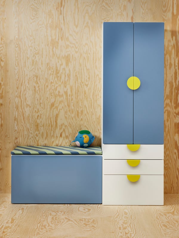 Blue and white SMÅSTAD/PLATSA storage furniture for kids, and a BÄNKKAMRAT bench pad with a soft toy.