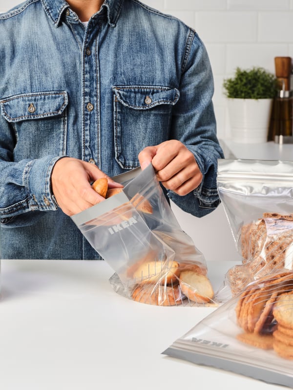 A white kitchen worktop, three ISTAD resealable bags and a person wearing a denim shirt putting rusks into one of the bags.