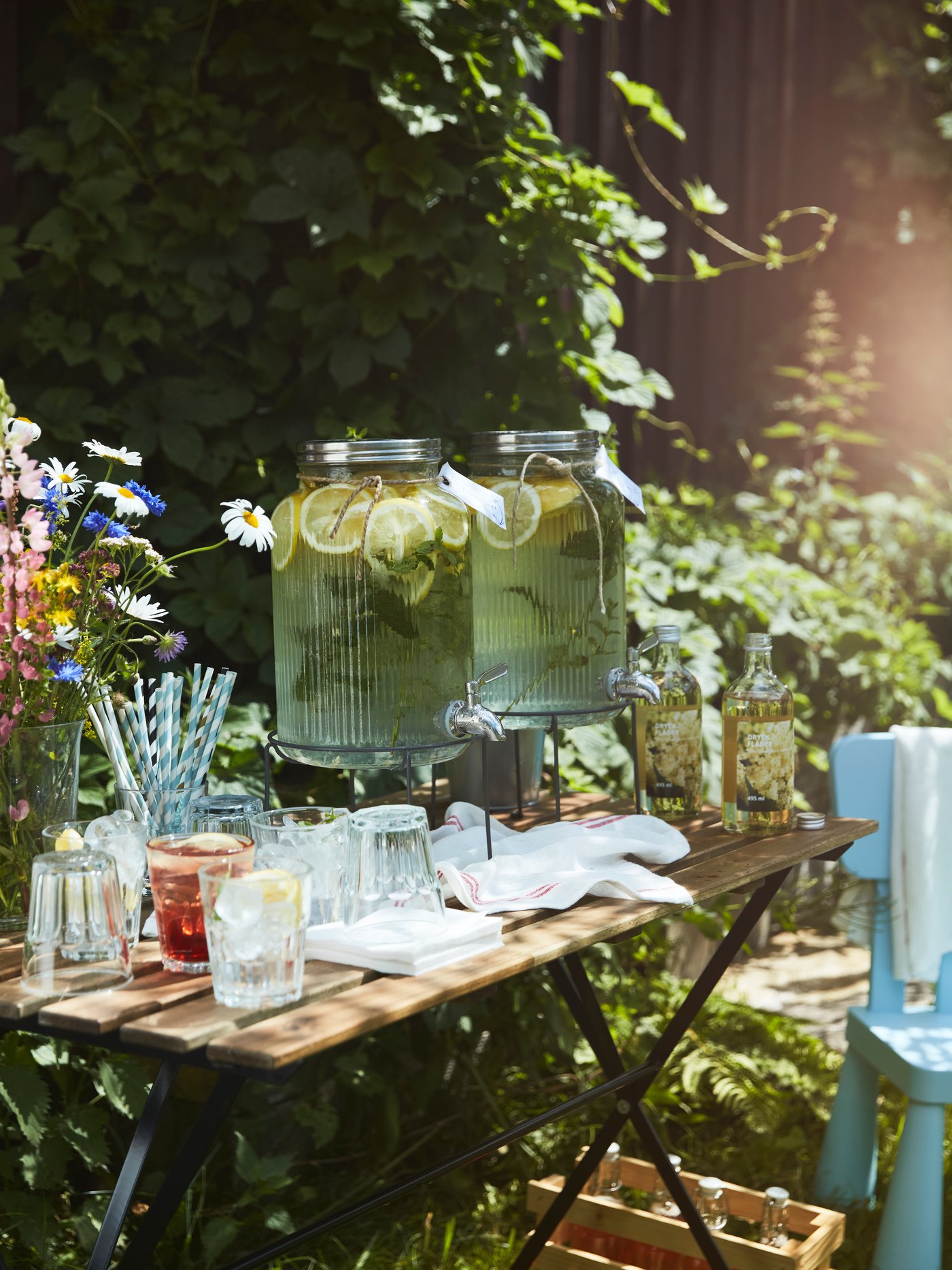 A small garden table set with glasses, straws, and lemonade in a VARDAGEN jar with tap, ready for guests at a party.