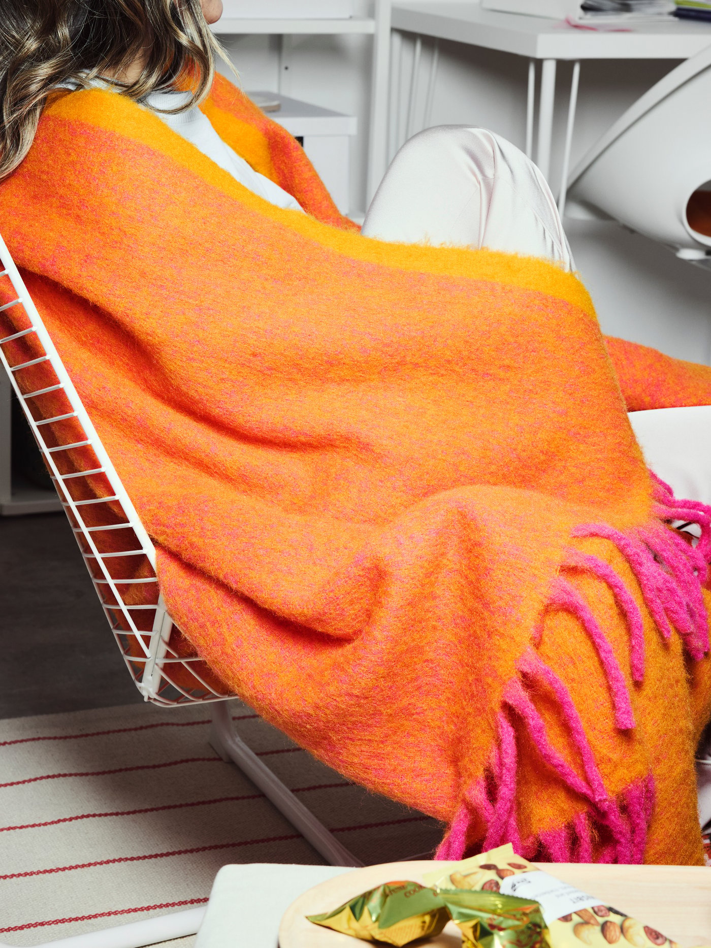 A person is wrapped in an orange/pink KLIPPOXEL throw.