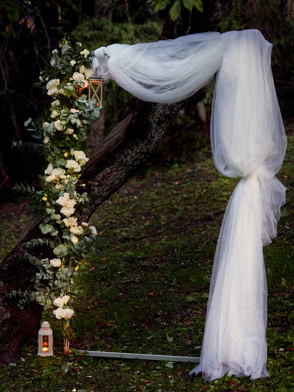 En stor ramme stå i en skov, og er bundet ind med tyl og blomster.
