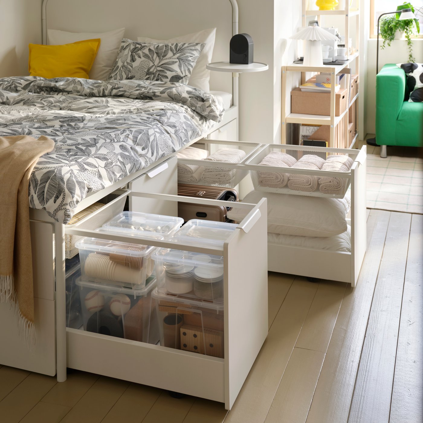 In un cassetto di una struttura letto bianca, alcuni contenitori con coperchio SAMLA in plastica trasparente al cui interno ci sono palle sportive e articoli per feste.